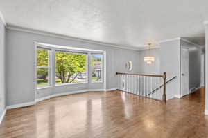 Unfurnished room with a textured ceiling, a chandelier, wood finished floors, ornamental molding, and baseboards