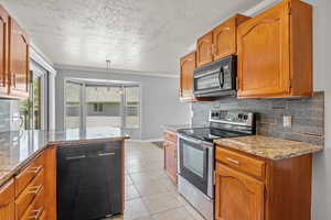 Kitchen featuring black appliances, decorative backsplash, plenty of natural light, brown cabinets, and crown molding