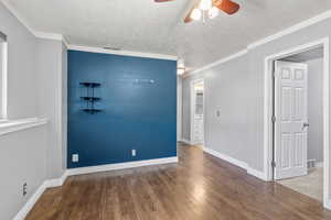 Unfurnished room with a ceiling fan, wood finished floors, a textured ceiling, baseboards, and ornamental molding
