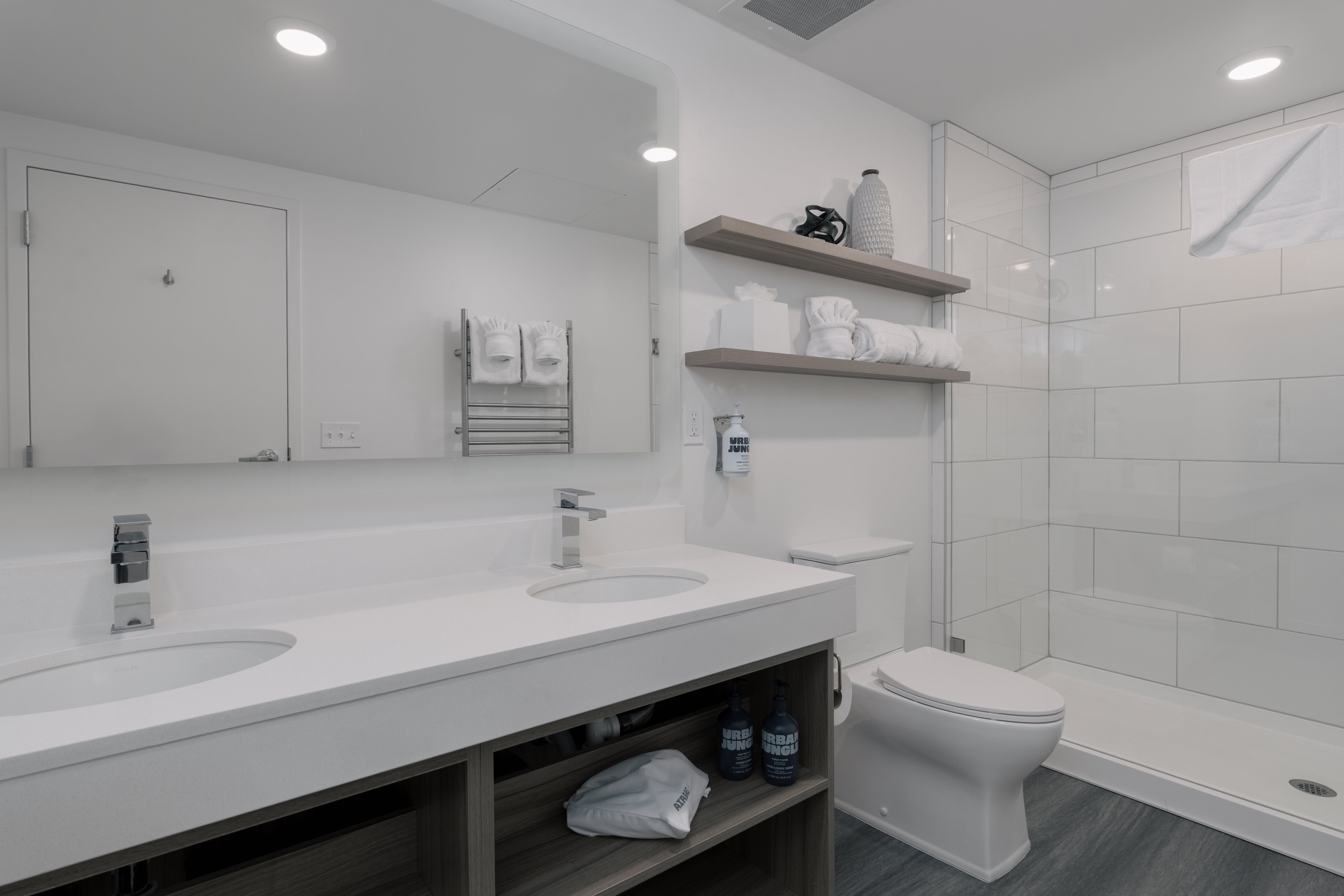 Bathroom featuring toilet, double vanity, a tile shower, wood finished floors, and recessed lighting
