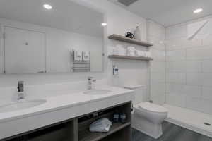 Bathroom featuring toilet, double vanity, a tile shower, wood finished floors, and recessed lighting