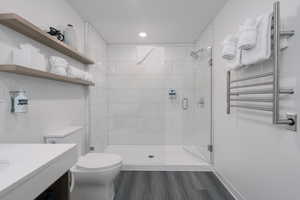 Bathroom with radiator, toilet, a stall shower, wood finished floors, and vanity