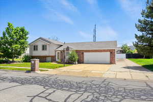 Split level home with driveway, a garage, brick siding, and a shingled roof