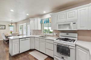 Kitchen with white appliances, a sink, a peninsula, white cabinetry, and recessed lighting