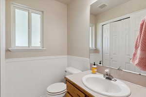 Half bath featuring a wainscoted wall, vanity, and toilet
