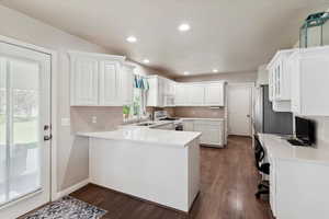 Kitchen featuring white appliances, white cabinets, a sink, a peninsula, and dark wood-style flooring