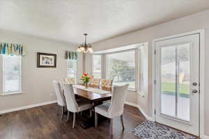 Dining room featuring a chandelier, a textured ceiling, dark wood-style floors, plenty of natural light, and baseboards