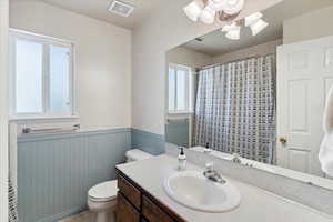 Bathroom featuring a wainscoted wall, toilet, vanity, a shower with curtain, and a chandelier
