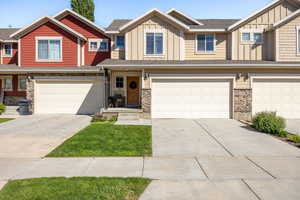 View of property with board and batten siding, stone siding, an attached garage, and concrete driveway
