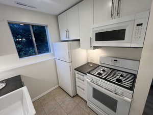 Kitchen featuring white appliances, white cabinets, dark countertops, and light tile patterned floors