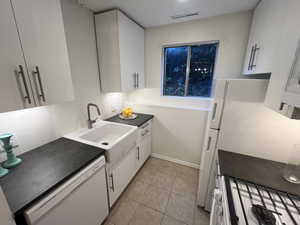 Kitchen with white appliances, white cabinets, light tile patterned floors, and dark countertops