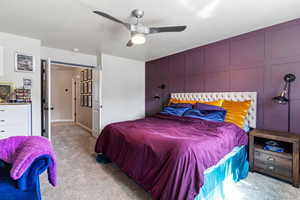 Carpeted bedroom featuring ceiling fan and a decorative wall