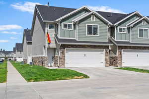 Townhome / multi-family property featuring stone siding, board and batten siding, a garage, driveway, and a front lawn