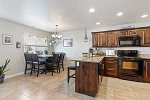 Kitchen with black appliances, a peninsula, a chandelier, a sink, and baseboards