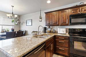 Kitchen with black appliances, a sink, a chandelier, a peninsula, and light stone countertops
