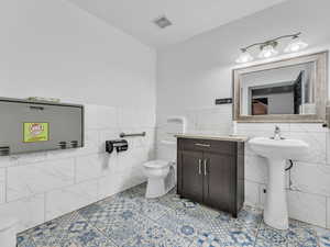 Bathroom with toilet, tile walls, a wainscoted wall, and a sink