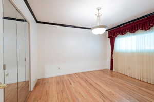 Unfurnished bedroom with wood finished floors, baseboards, crown molding, and a closet