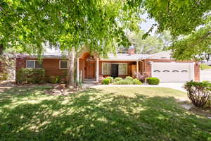 Ranch-style home with brick siding, a garage, a front yard, and a chimney