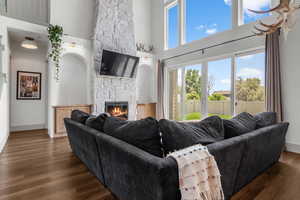 Living room with a stone fireplace, a high ceiling, dark wood-type flooring, and baseboards