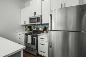 Apartment kitchen featuring stainless steel appliances, a sink, tile backsplash, a breakfast bar, and dark wood-style LVT floors