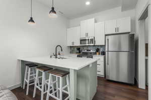 Apartment kitchen featuring stainless steel appliances, a sink, tile backsplash, a breakfast bar, and dark wood-style LVT floors