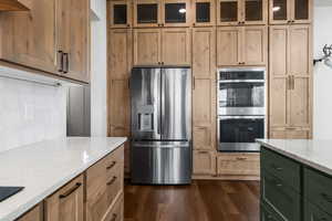 Kitchen featuring appliances with stainless steel finishes, tasteful tile backsplash, Taj-Mahal quartzite countertops, and glass insert  custom cabinets