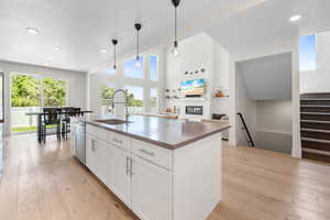 Kitchen with a sink, stainless steel dishwasher, light wood-type flooring, hanging light fixtures, and a glass covered fireplace