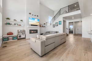 Living area featuring a high ceiling, a glass covered fireplace, light wood-style floors, and baseboards