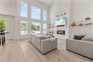 Living area featuring light wood finished floors, a glass covered fireplace, a towering ceiling, and baseboards