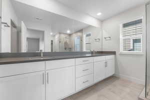 Full bath with double vanity, baseboards, a shower stall, and recessed lighting