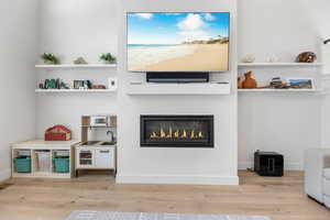 Living area with light wood-style floors, a glass covered fireplace, and baseboards