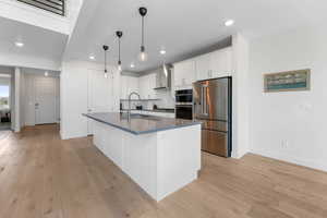 Kitchen with stainless steel appliances, wall chimney range hood, dark countertops, recessed lighting, and white cabinetry