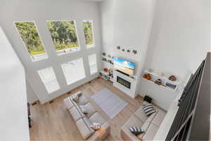 Living room with a towering ceiling, healthy amount of natural light, a glass covered fireplace, and wood finished floors