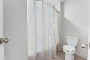 Bathroom with toilet, baseboards, and curtained shower