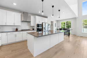 Kitchen featuring wall chimney range hood, appliances with stainless steel finishes, light wood-type flooring, dark countertops, and recessed lighting