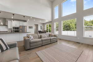 Living room with healthy amount of natural light, light wood-style floors, a high ceiling, baseboards, and recessed lighting