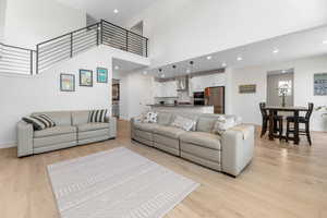 Living room with light wood finished floors, a high ceiling, baseboards, recessed lighting, and stairs