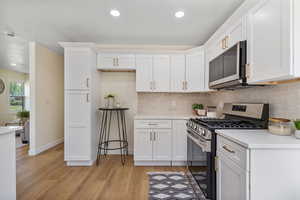 Kitchen featuring appliances with stainless steel finishes, light wood-style floors, white cabinetry, light countertops, and decorative backsplash