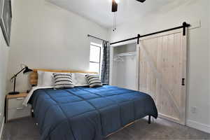 Carpeted bedroom featuring a barn door, a closet, a ceiling fan, and baseboards