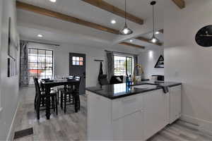 Kitchen featuring a sink, light wood-style floors, baseboards, dishwasher, and beam ceiling
