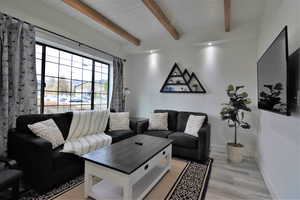 Living area with light wood-style floors, beam ceiling, and baseboards