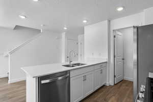Kitchen with appliances with stainless steel finishes, a sink, a peninsula, wood finished floors, and light countertops