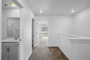 Corridor featuring a sink, dark colored carpet, baseboards, and recessed lighting