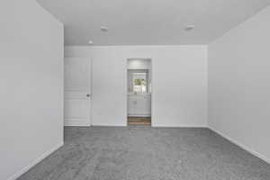 Unfurnished bedroom featuring carpet, baseboards, ensuite bathroom, and a textured ceiling
