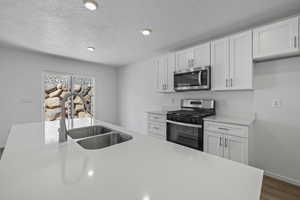 Kitchen with appliances with stainless steel finishes, a sink, light countertops, white cabinets, and a textured ceiling