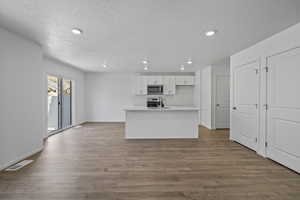 Kitchen with stainless steel microwave, recessed lighting, white cabinetry, light countertops, and wood finished floors