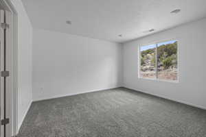 Carpeted empty room with a textured ceiling and baseboards