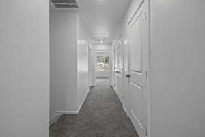 Hall featuring dark carpet, baseboards, a textured ceiling, and attic access