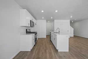 Kitchen with a sink, appliances with stainless steel finishes, baseboards, wood finished floors, and recessed lighting