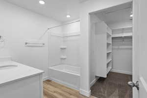 Bathroom featuring shower / tub combination, vanity, wood finished floors, recessed lighting, and a spacious closet